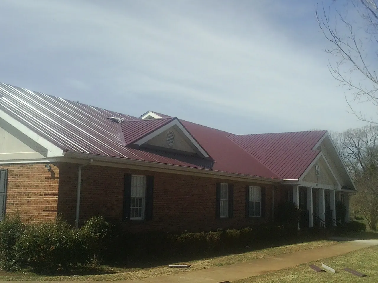 Red metal roof with gabled entries on a long brick building, from a Hail Damage Roof Repair job in Dana Point